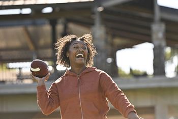 a woman holding a football in one hand and smiling in the other